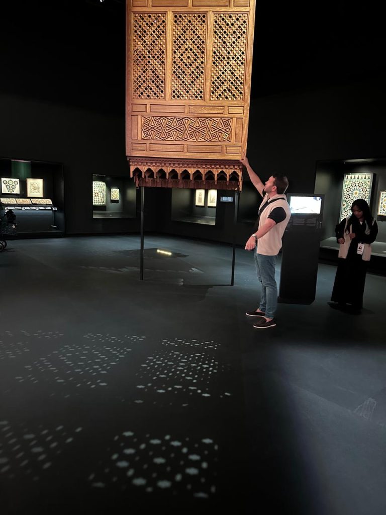 Sunlight filtering through ornate wooden lattice, creating geometric shadow patterns on the wall.