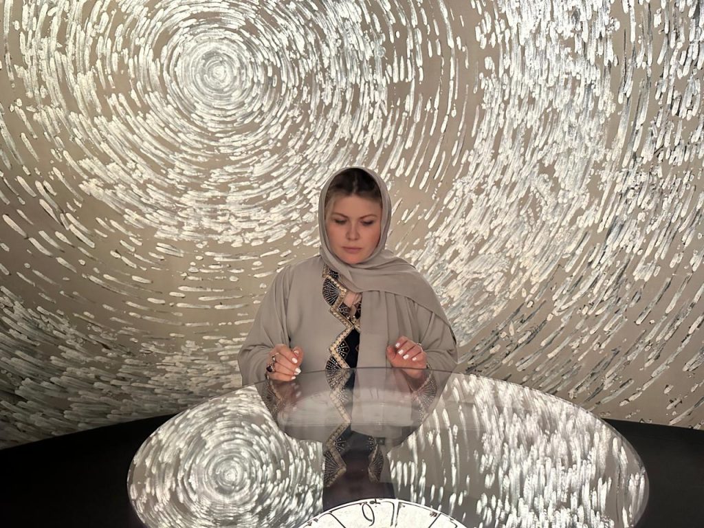 Woman in traditional attire seated at an artistic installation with swirling circular patterns