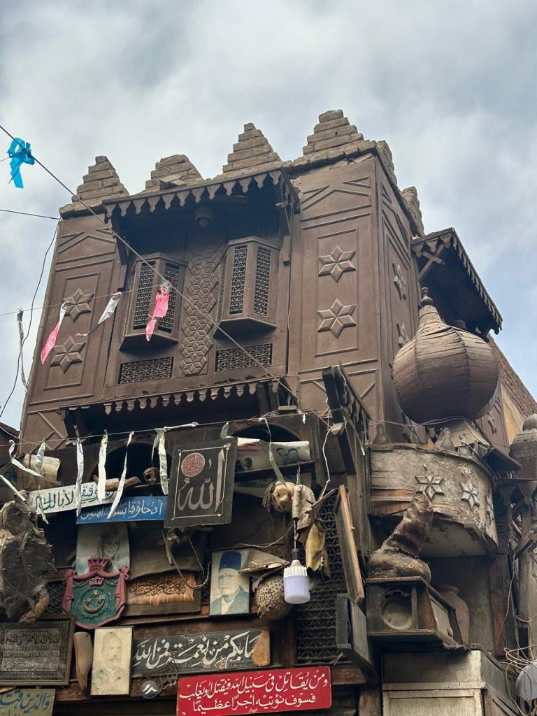 Close-up of a historic wooden building in Cairo, featuring carved mashrabiya windows and an eclectic collection of signs and decorative objects