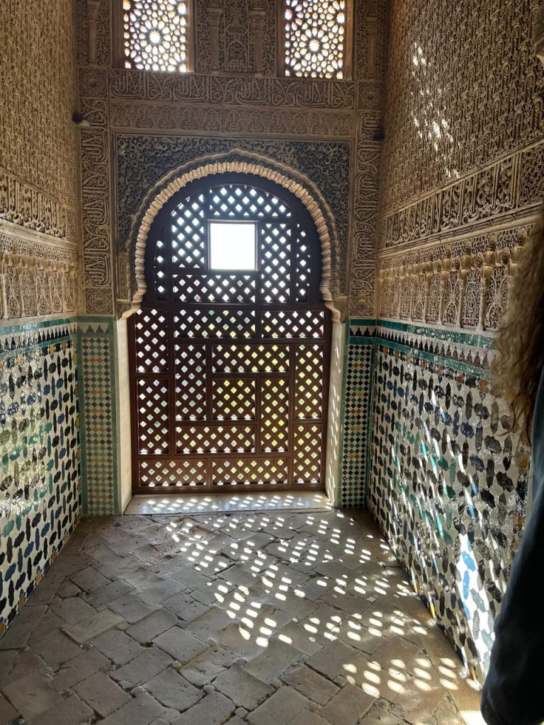  Intricate lattice window in the Alhambra, Granada, casting geometric light patterns on the floor.