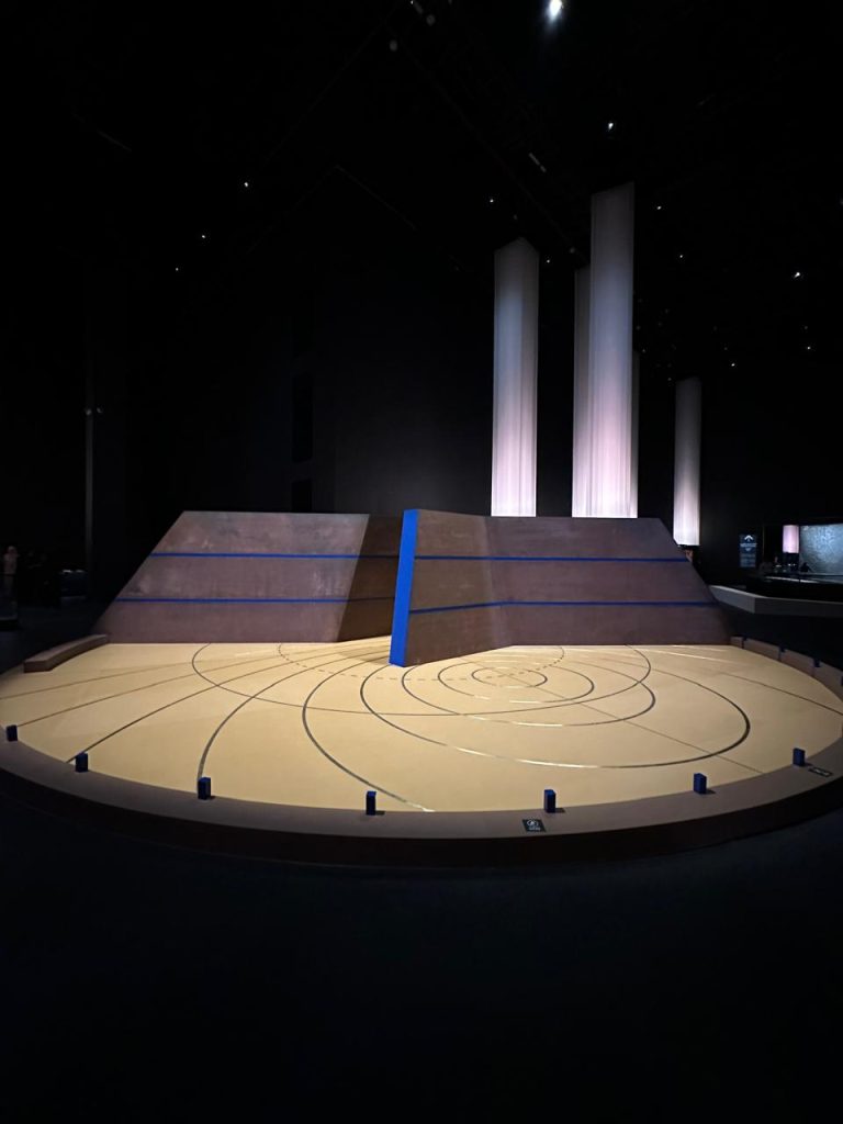 Modern exhibition installation featuring a large circular map with blue line, inspired by Islamic cosmology.
